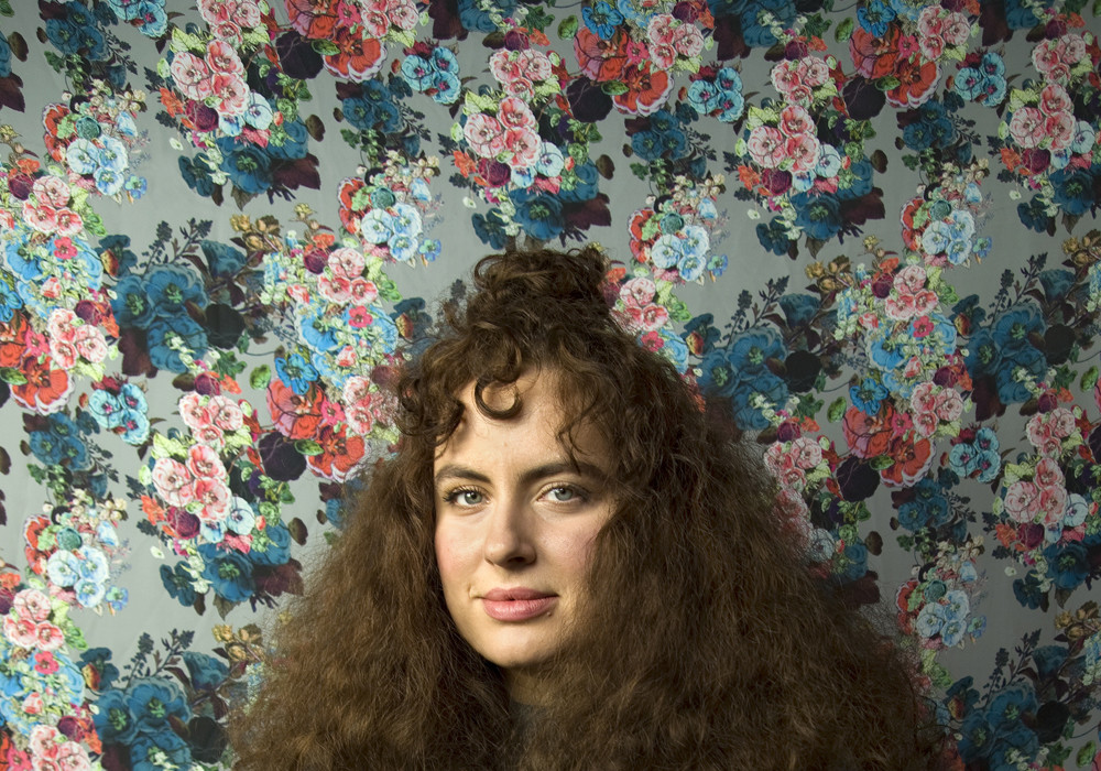 Woman with curly brown hair against a background print of roses. This art paper has a smooth surface and has been the number one choice for artists since its inception.